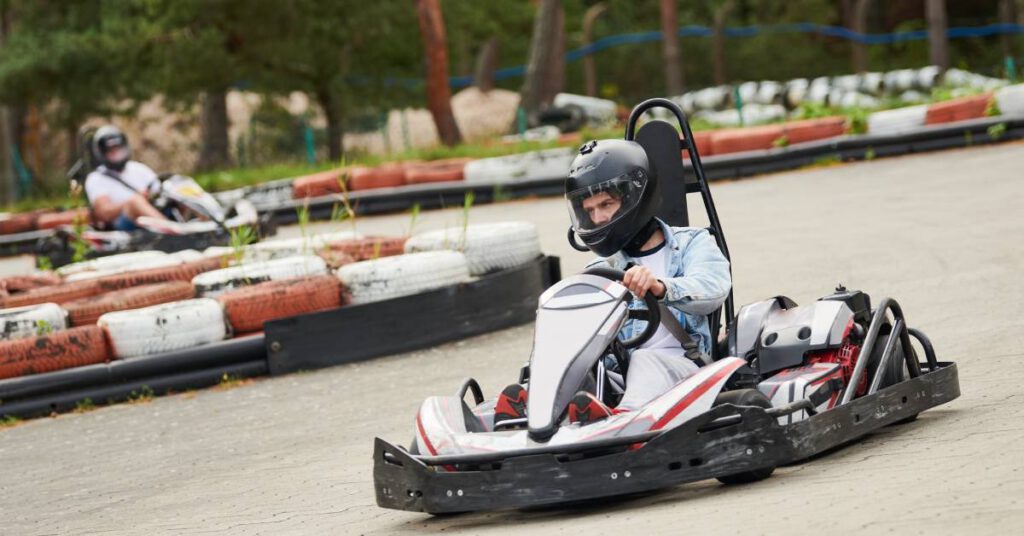 A man driving down the track in a white and red go-kart. He is focused on the road in front of him while turning.