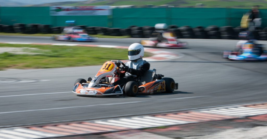 A racer in a black suit speeding through a corner in kart number 31 on an outdoor track with tire walls and banners.