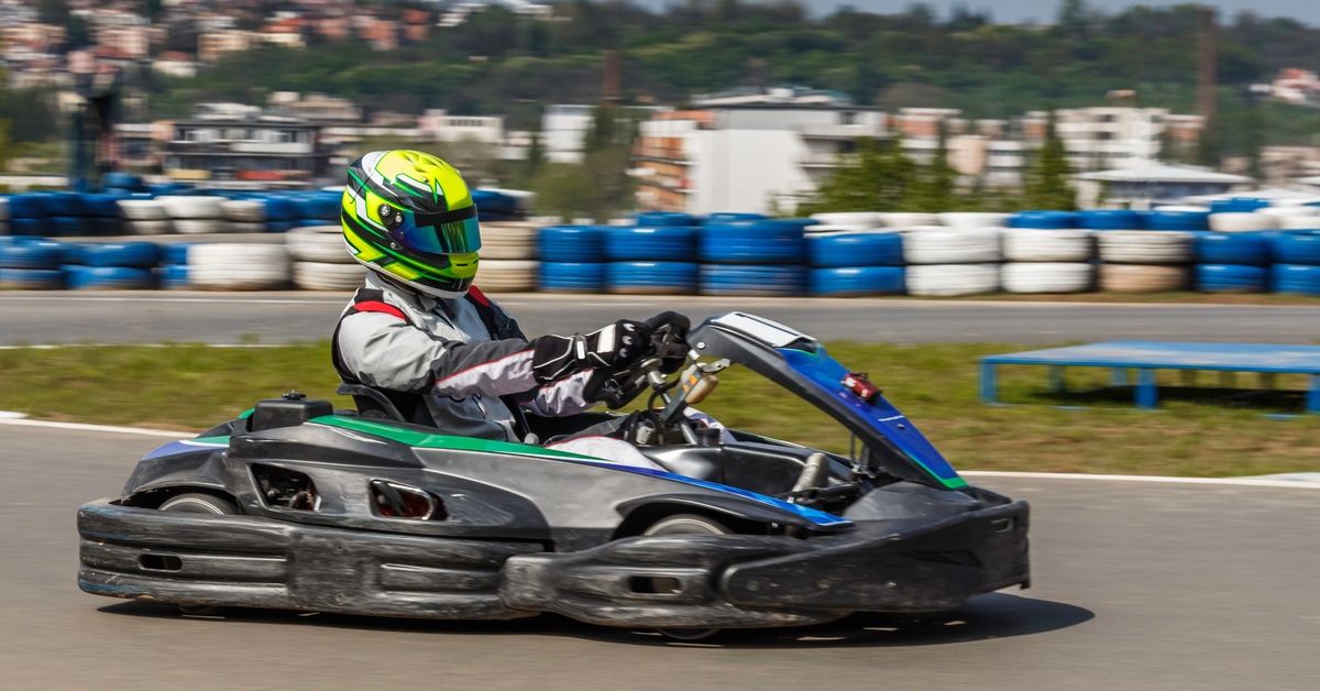 A driver in a green helmet and racing suit driving a black go-kart along a curved section of an outdoor race circuit.