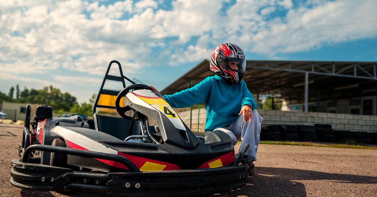 Person in a red helmet sitting on the edge of a black go-kart with a yellow number 4 on the front bumper.