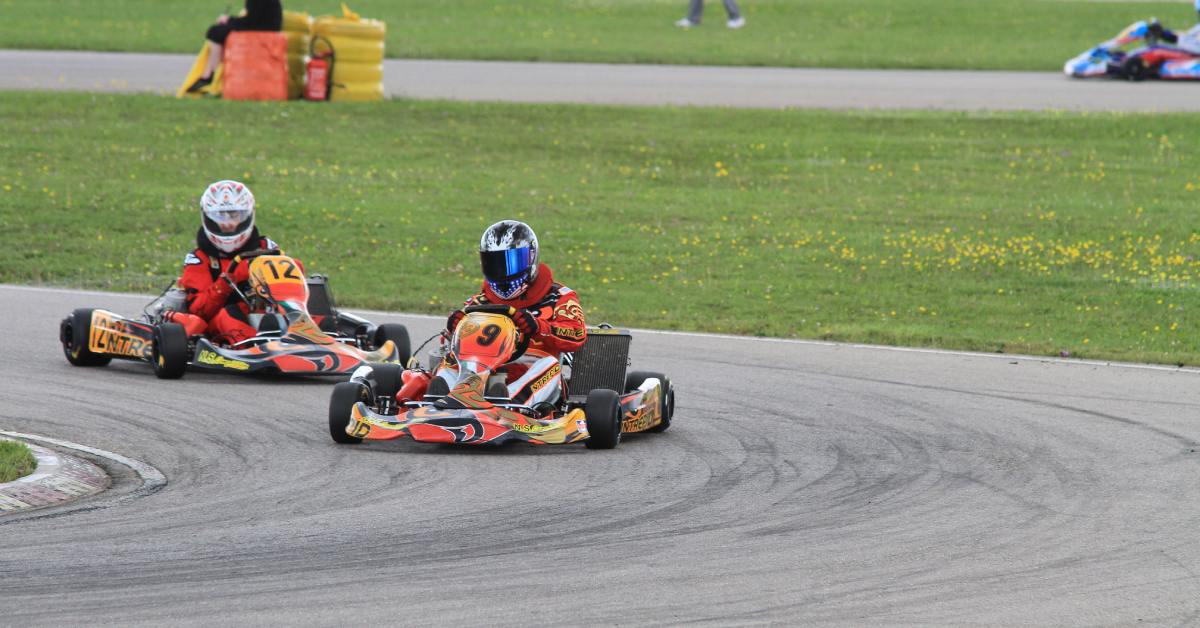 A person driving a go-kart, rounding a turn. There is another racer just behind them, also rounding the turn.