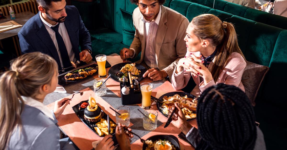 Business professionals in formal clothing sitting around a restaurant table with meals and drinks during a business meeting.