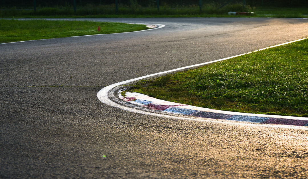 A close-up view shows a turn on an outdoor go-kart track. Grass sits on either side of the outdoor track.